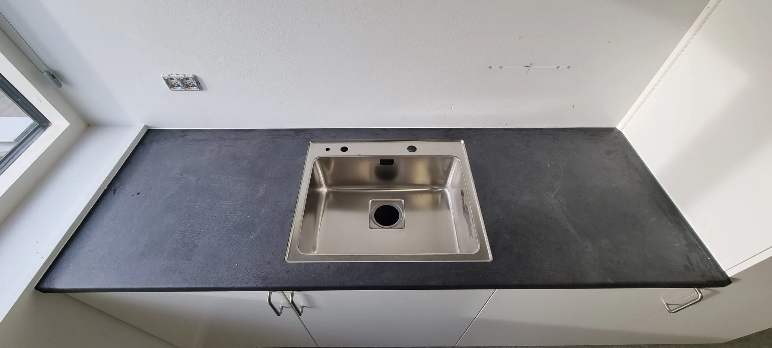 Lang, sort bordplade med stålvask og en ny fuge mod væggen