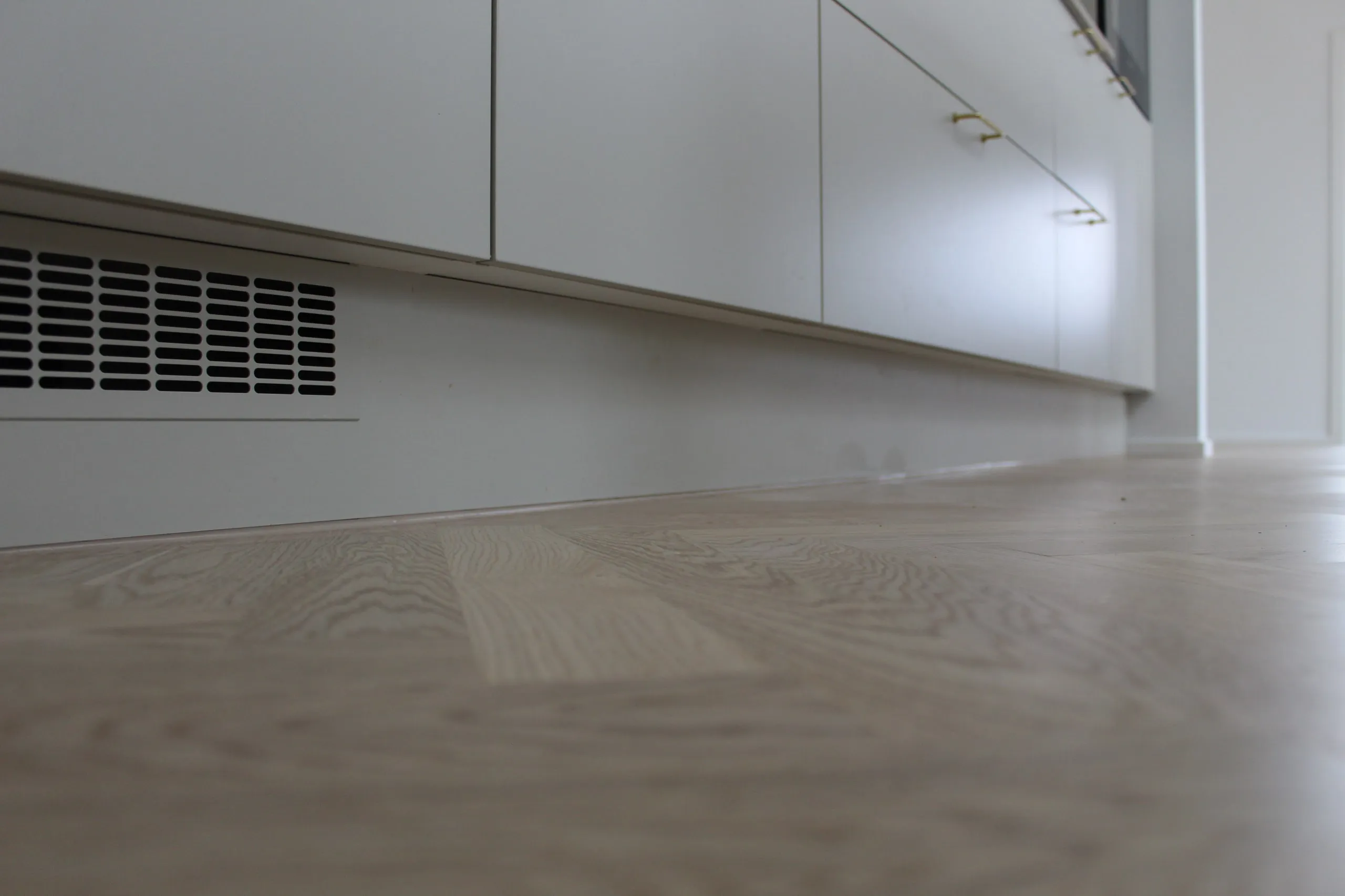 Lyse køkkenskabe med ventilationsrist i soklen og ny fuge mod gulvet